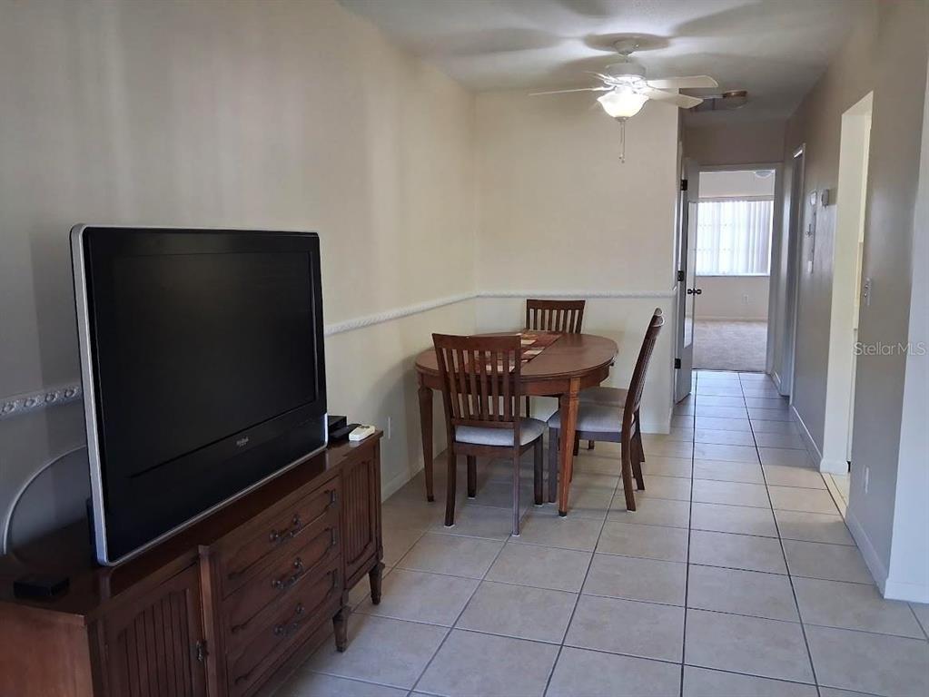 A dining area with a wooden table and chairs sits next to a television console — 4744 AZALEA DRIVE UNIT 204, NEW PORT RICHEY, FL