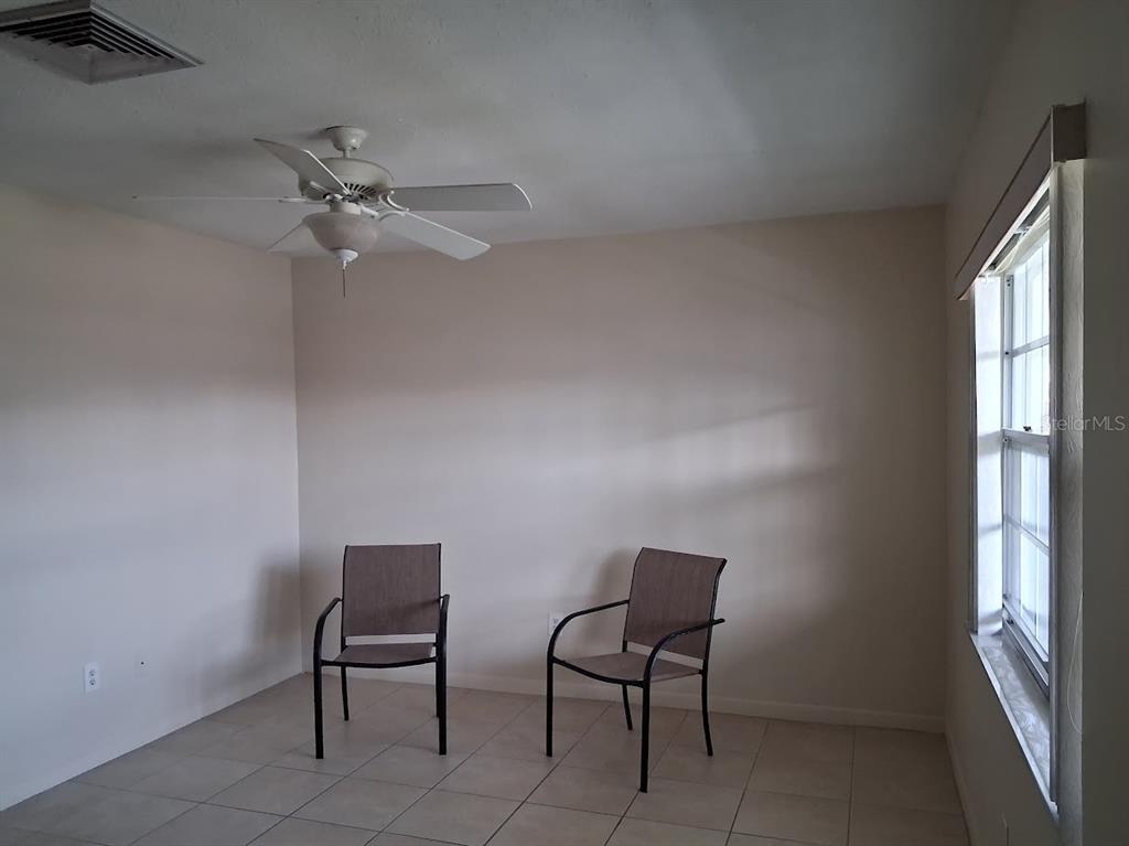 An empty room with light-colored walls, tile flooring, a ceiling fan, and two chairs — 4744 AZALEA DRIVE UNIT 204, NEW PORT RICHEY, FL