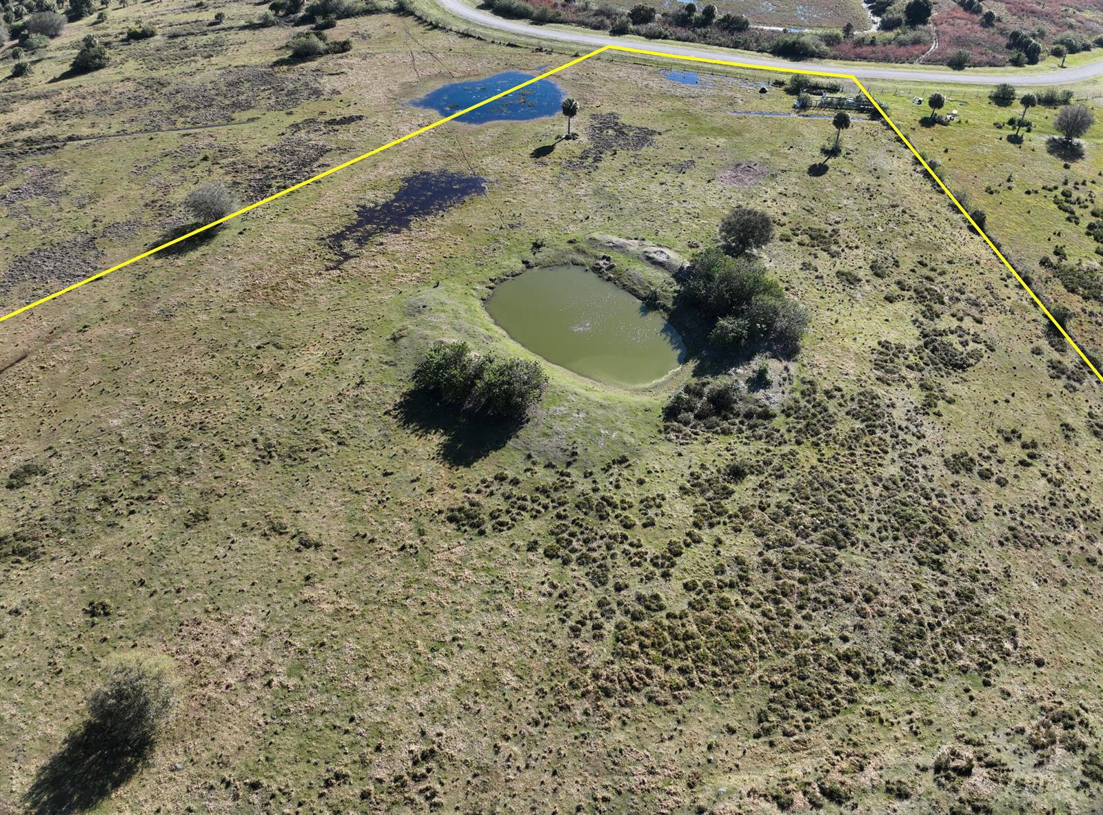 An aerial view shows a rural lot with a pond, scattered trees, and yellow boundary lines — 6584 SE 26th Trail, Okeechobee FL 34974, OKEECHOBEE, FL