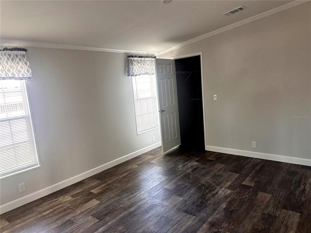 A bedroom with gray walls, dark wood-look flooring, two windows, and an open closet door — 3428 GREENBLUFF ROAD UNIT 1135, ZELLWOOD, FL