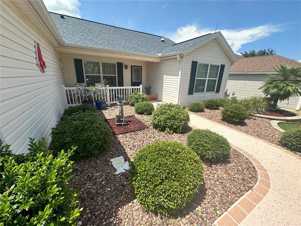 The exterior of a house features beige siding, a shingled roof, and a landscaped yard — 1515 BAYLOR PLACE, THE VILLAGES, FL