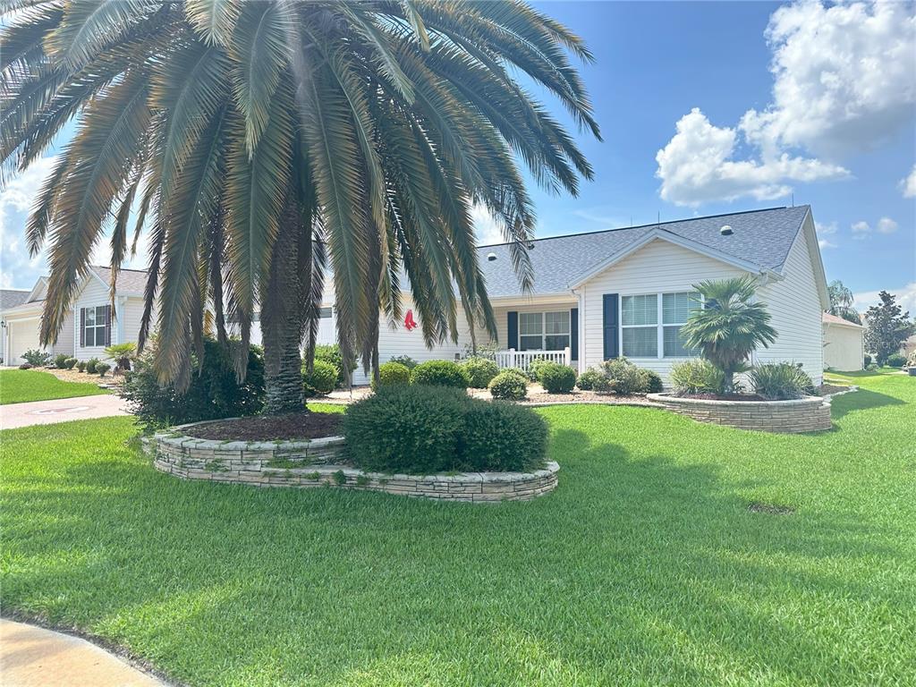 A single-story house with white siding, a large palm tree, and stone-bordered landscaping — 1515 BAYLOR PLACE, THE VILLAGES, FL