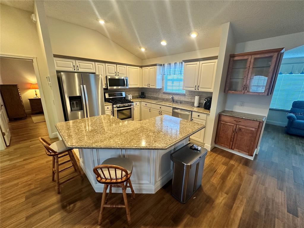 A kitchen features white cabinets, granite countertops, a stainless steel refrigerator, and wood-look flooring — 1515 BAYLOR PLACE, THE VILLAGES, FL