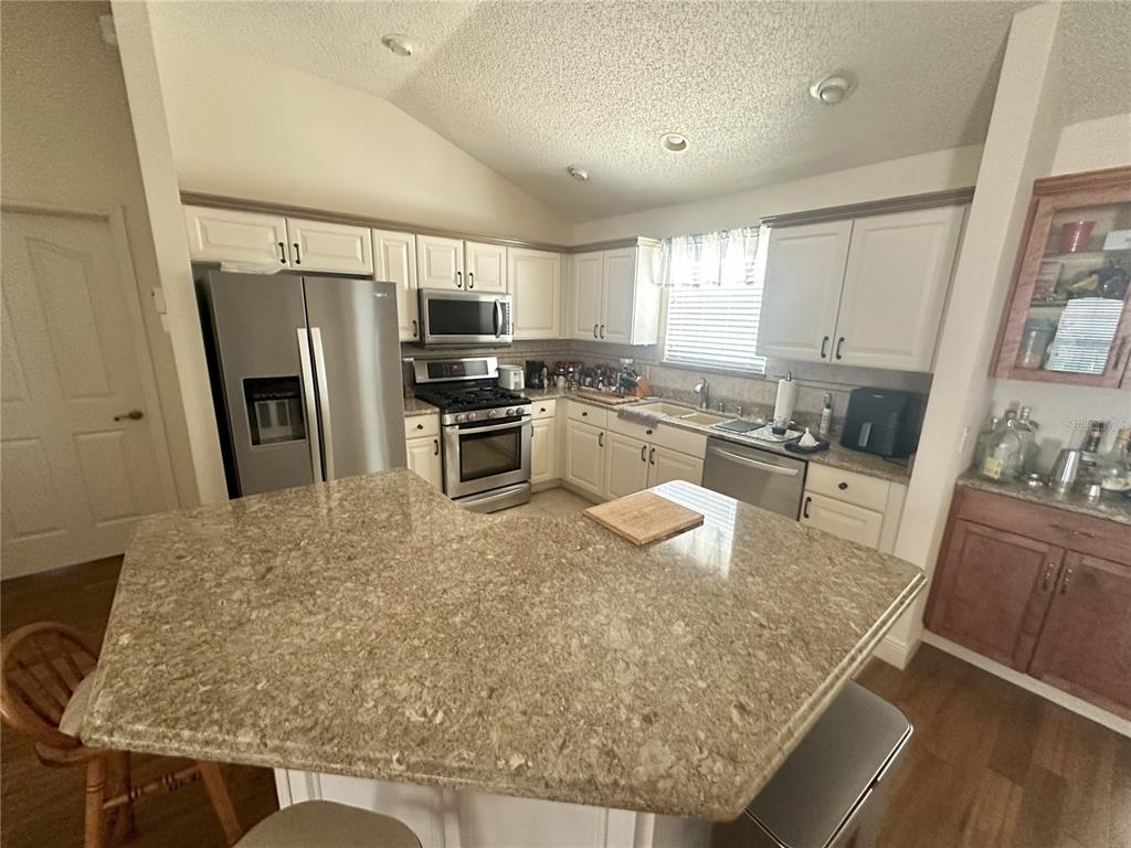 A kitchen features white cabinets, granite countertops, stainless steel appliances, and a central island — 1515 BAYLOR PLACE, THE VILLAGES, FL
