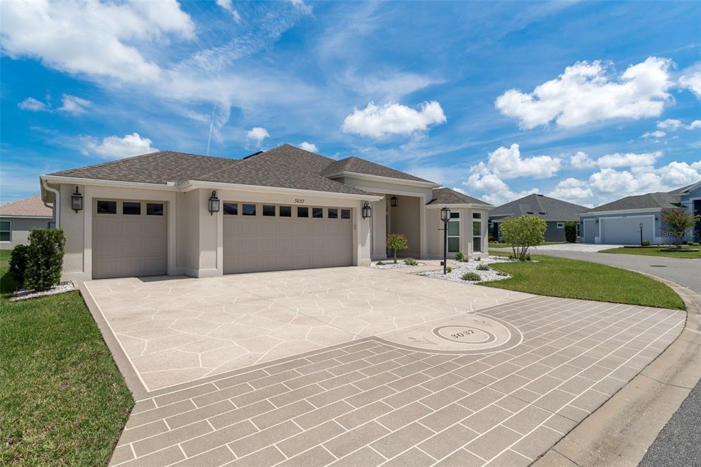 A single-story house with a beige exterior, a three-car garage, and a decorative paved driveway — 3037 LICCIARDELLO PATH, THE VILLAGES, FL