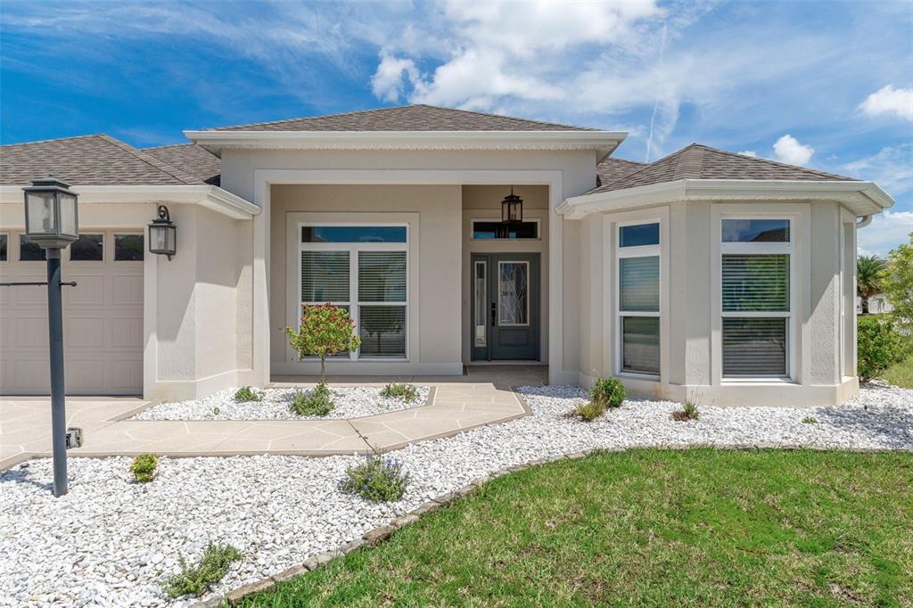 The exterior of a single-story house features a gray front door, white stucco, and gravel — 3037 LICCIARDELLO PATH, THE VILLAGES, FL