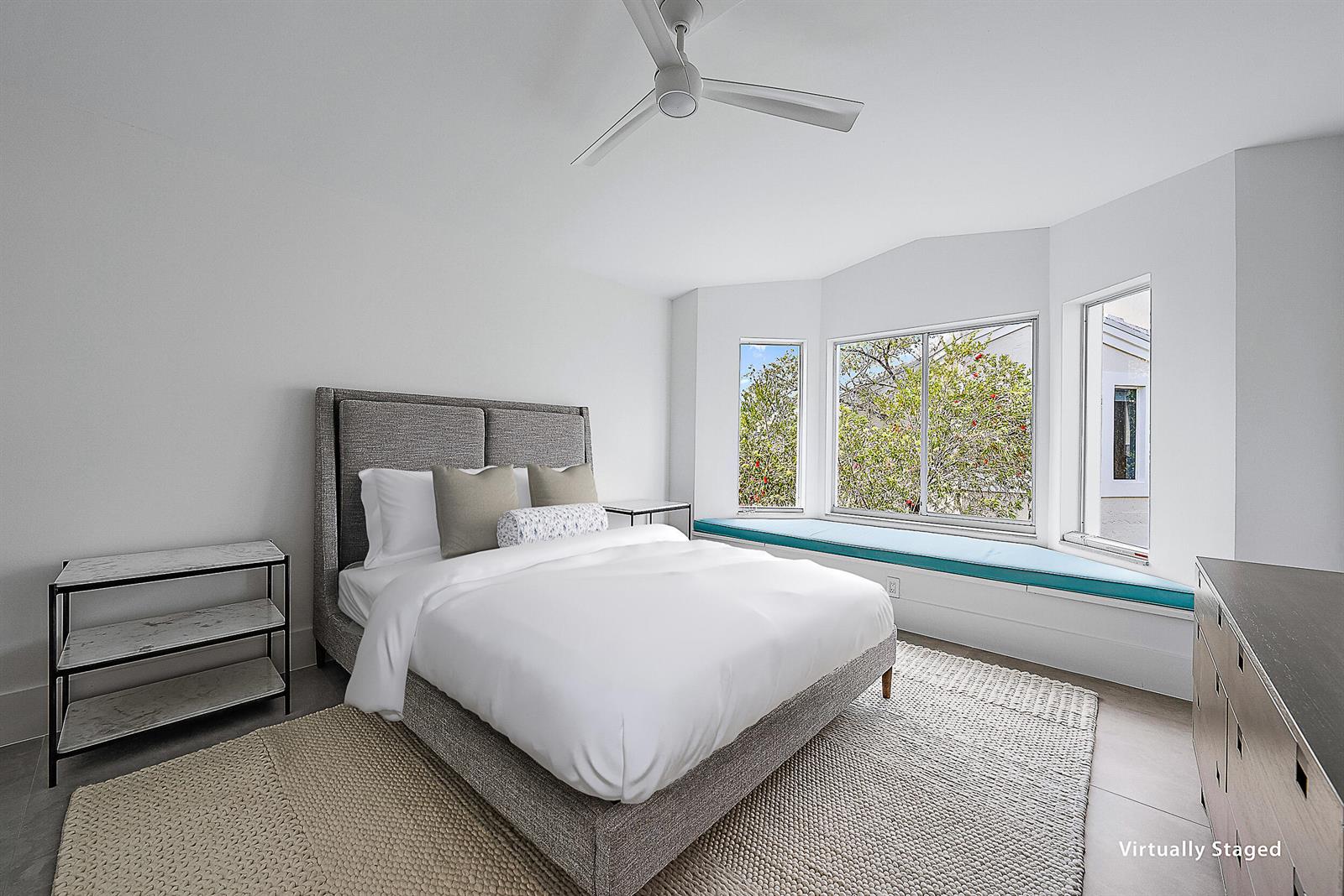 A bedroom with a gray upholstered bed, white walls, and a window seat with cushions — 802 Captains Way, Jupiter FL 33477, JUPITER, FL