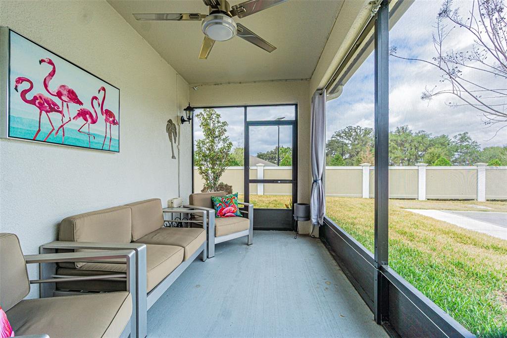 A screened-in patio features tan outdoor furniture, a flamingo wall print, and a ceiling fan — 31310 CABANA RYE AVENUE, SAN ANTONIO, FL