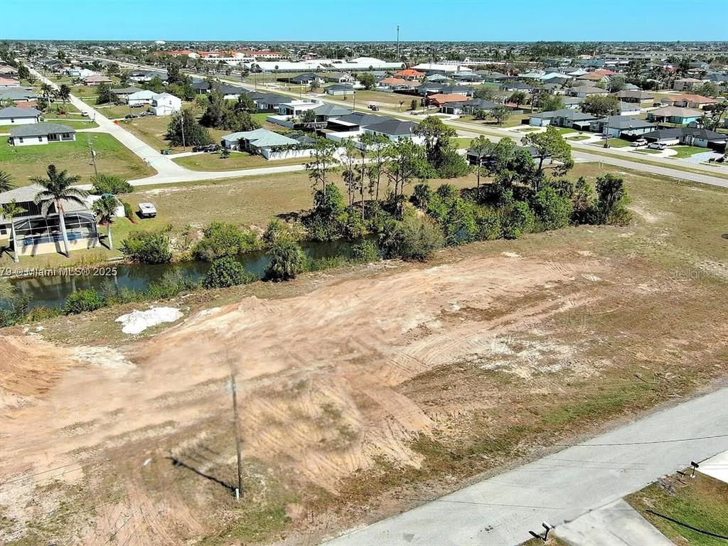 An aerial view shows a cleared, vacant residential lot adjacent to a canal and road — 1611 NW 2ND STREET, CAPE CORAL, FL