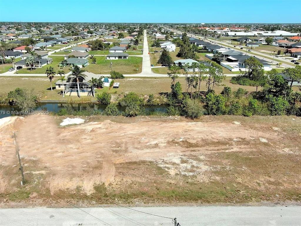 An aerial view shows a cleared, sandy vacant lot bordering a canal and residential neighborhood — 1611 NW 2ND STREET, CAPE CORAL, FL