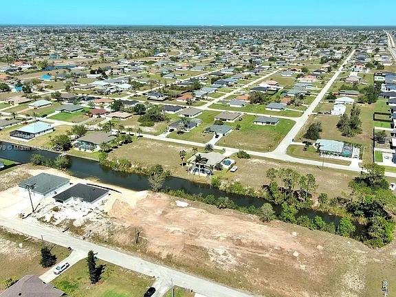 This aerial view shows a residential neighborhood with houses, a canal, and vacant lots — 1611 NW 2ND STREET, CAPE CORAL, FL