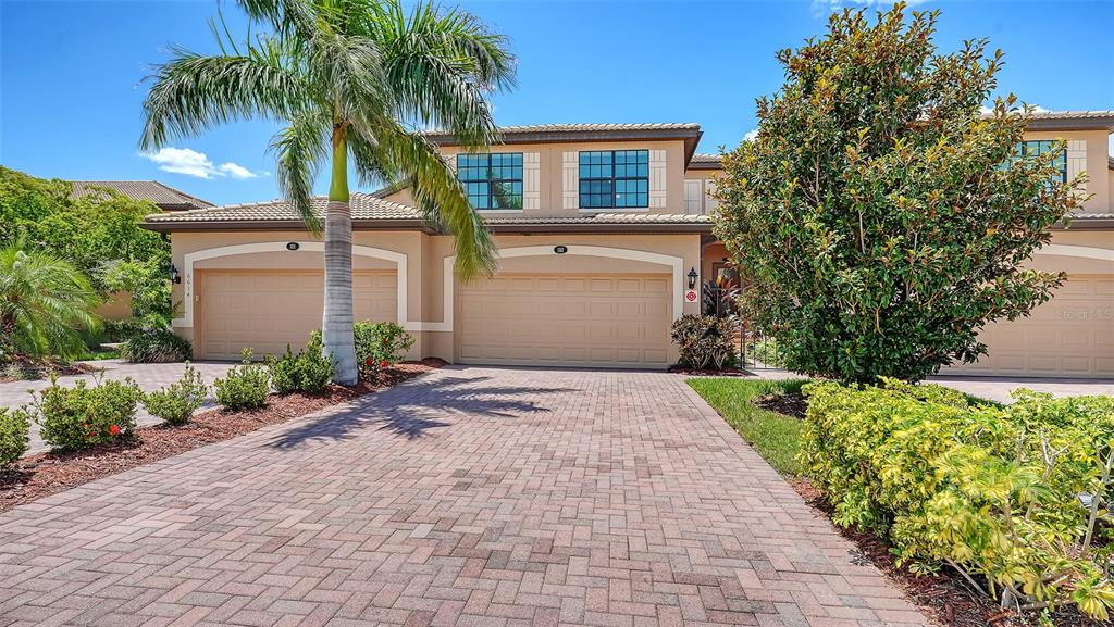 A two-story house with a paved driveway, three garage doors, and a palm tree — 6614 GRAND ESTUARY TRAIL UNIT 102, BRADENTON, FL