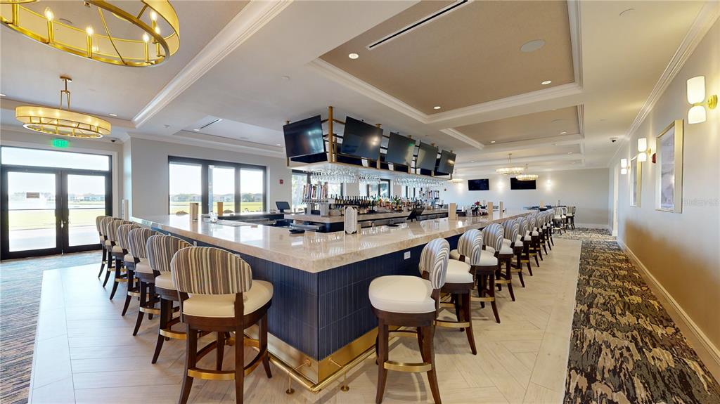A modern bar area features a large central counter with stools and overhead televisions — 6614 GRAND ESTUARY TRAIL UNIT 102, BRADENTON, FL