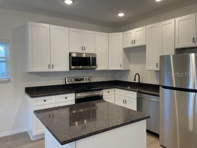 A kitchen features white cabinets, dark granite countertops, stainless steel appliances, and a center island — 1482 CLEVELAND STREET, CLEARWATER, FL