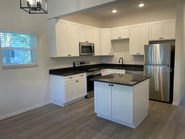 A kitchen features white cabinets, stainless steel appliances, a center island, and light wood flooring — 1482 CLEVELAND STREET, CLEARWATER, FL