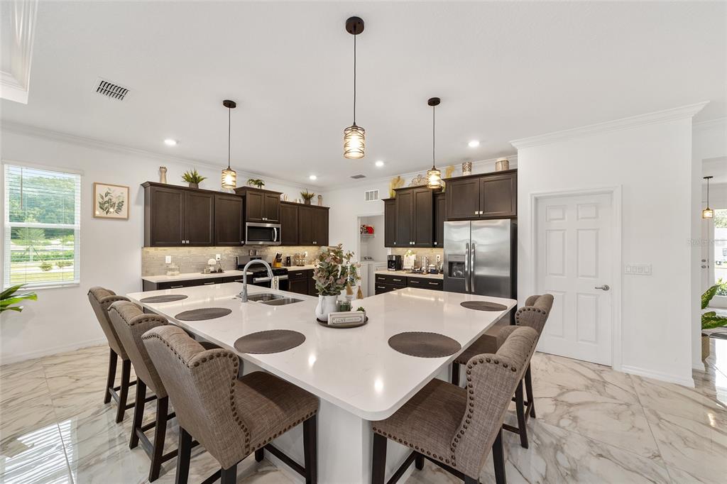 A kitchen features dark wood cabinets, a large white quartz island, and marble-look tile flooring — 7037 SW 86TH AVENUE, OCALA, FL