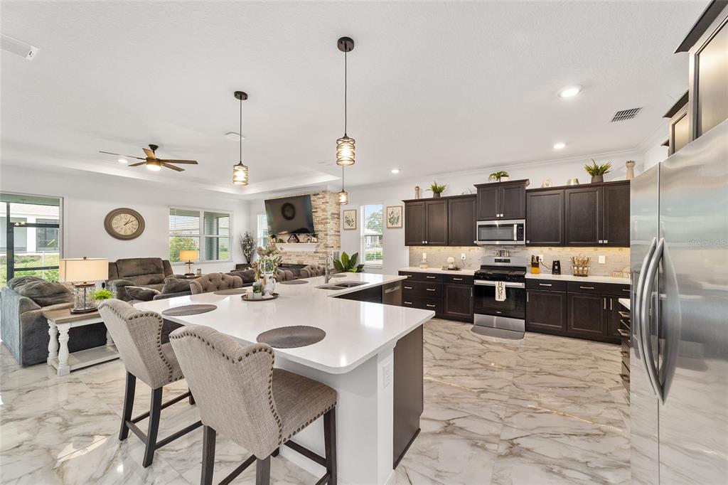 A modern open-concept kitchen features dark cabinetry, white quartz countertops, and marble-patterned tile flooring — 7037 SW 86TH AVENUE, OCALA, FL