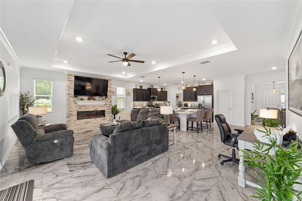 An open-concept living room and kitchen feature marble-look tile floors and a stone fireplace — 7037 SW 86TH AVENUE, OCALA, FL