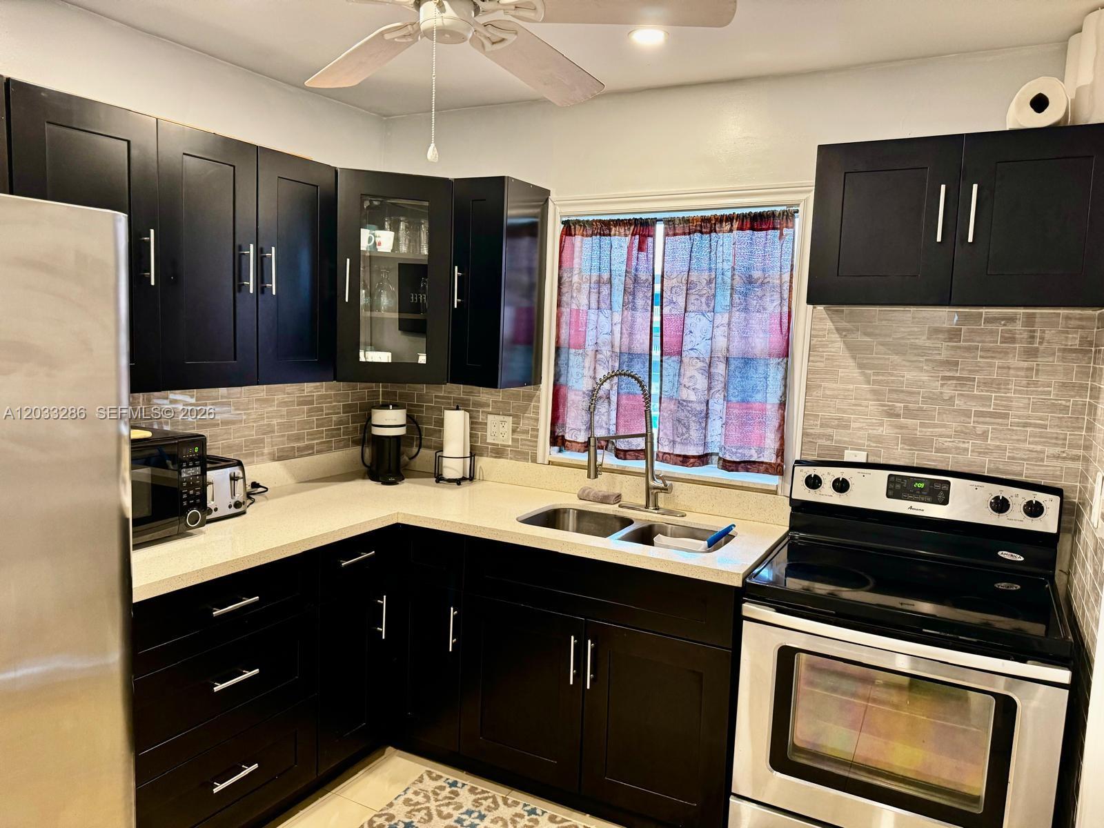 A kitchen features dark cabinets, light countertops, a tiled backsplash, and stainless steel appliances — 5300 Washington St # H236, Hollywood FL 33021, HOLLYWOOD, FL