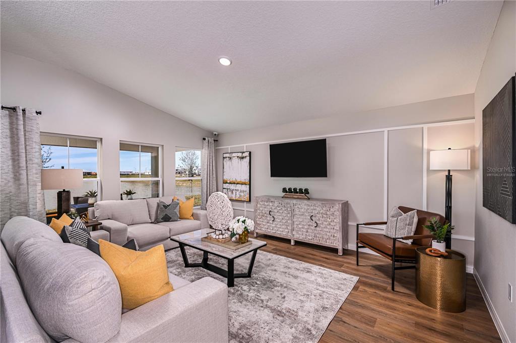 A living room features a gray sofa, a brown leather chair, and a wall-mounted television — 2330 STILLVIEW PASS, ZEPHYRHILLS, FL