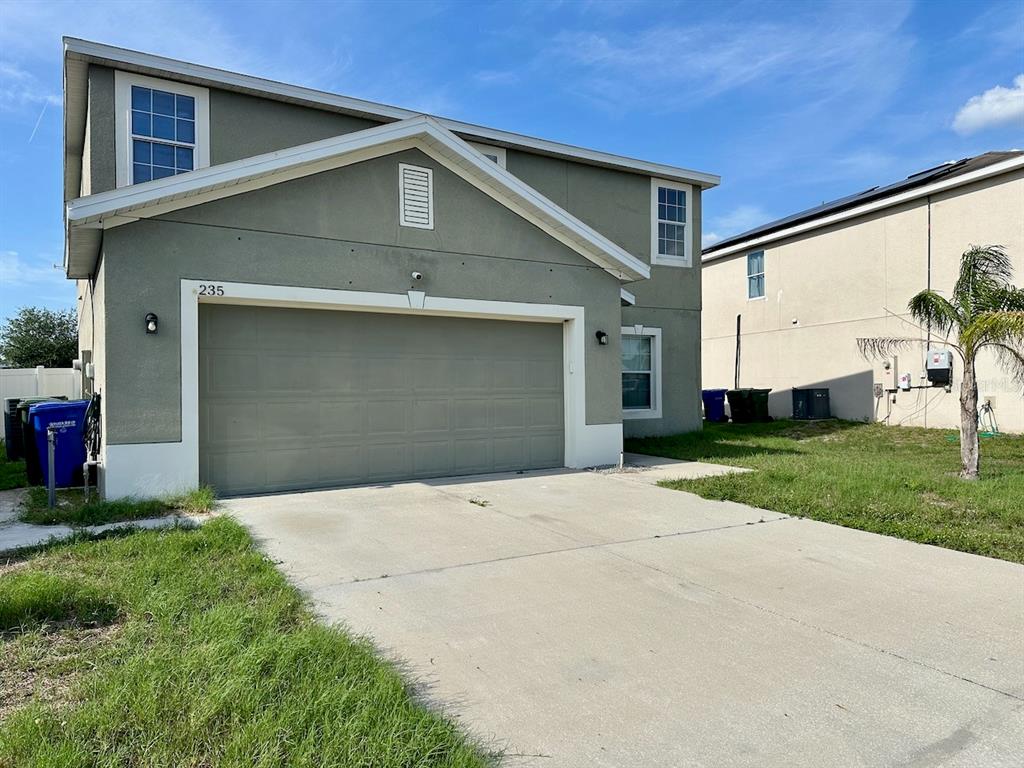 A two-story house with a beige stucco exterior, a two-car garage, and a concrete driveway — 235 HIBISCUS STREET, WINTER HAVEN, FL