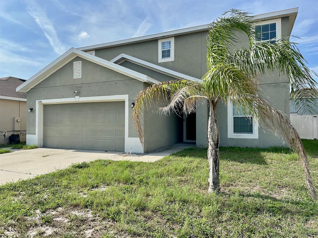 A two-story house with a beige stucco exterior, a two-car garage, and a palm tree — 235 HIBISCUS STREET, WINTER HAVEN, FL
