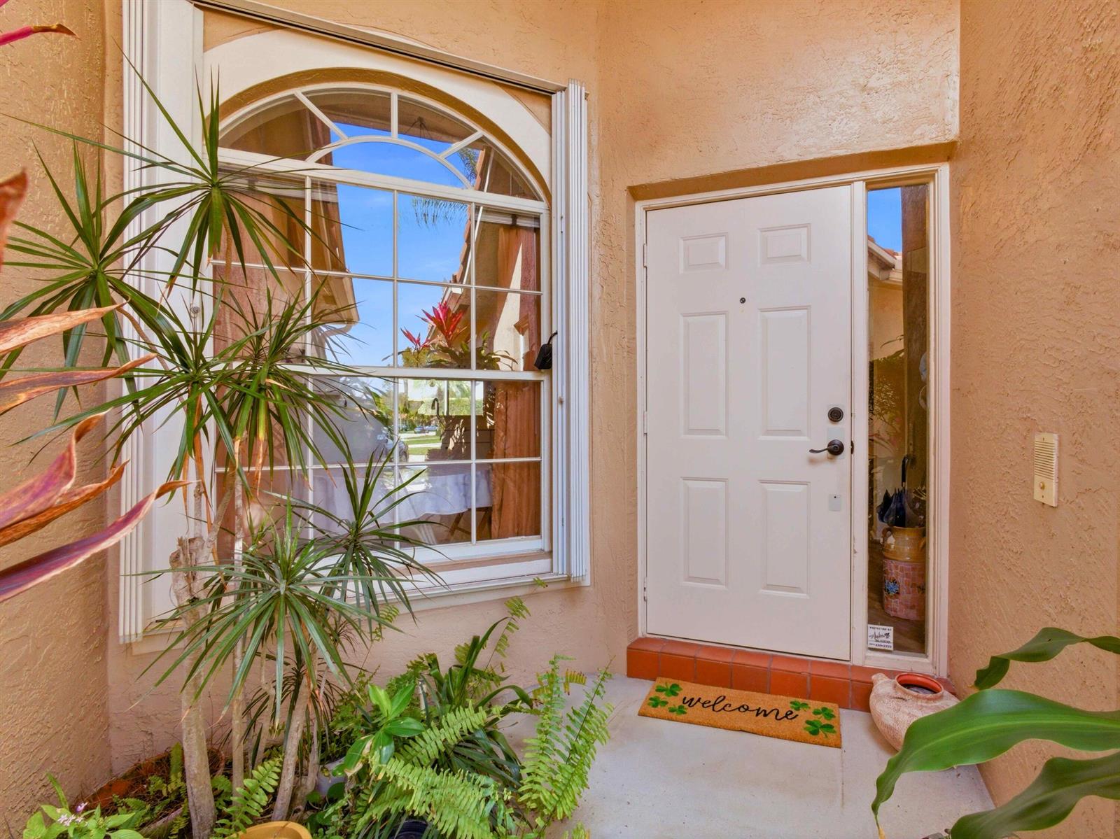 An exterior view of a front entryway with a white door, arched window, and potted plants — 6367 Long Key Lane, Boynton Beach FL 33472, BOYNTON BEACH, FL