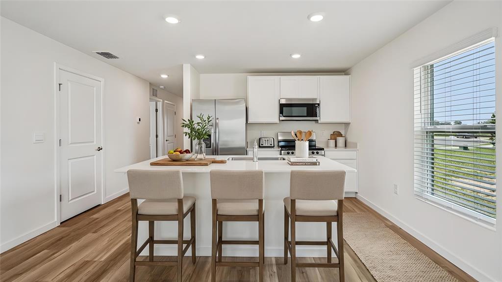 A modern kitchen features a white island with three stools, stainless steel appliances, and wood-look flooring — 7812 SW 46TH COURT, OCALA, FL