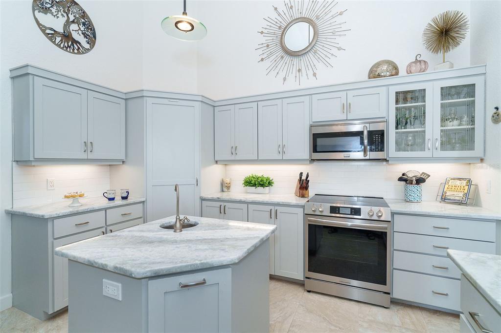 A kitchen features light blue cabinets, a marble-topped island with a sink, and stainless appliances — 100 N GREEN DOLPHIN DRIVE, CAPE HAZE, FL