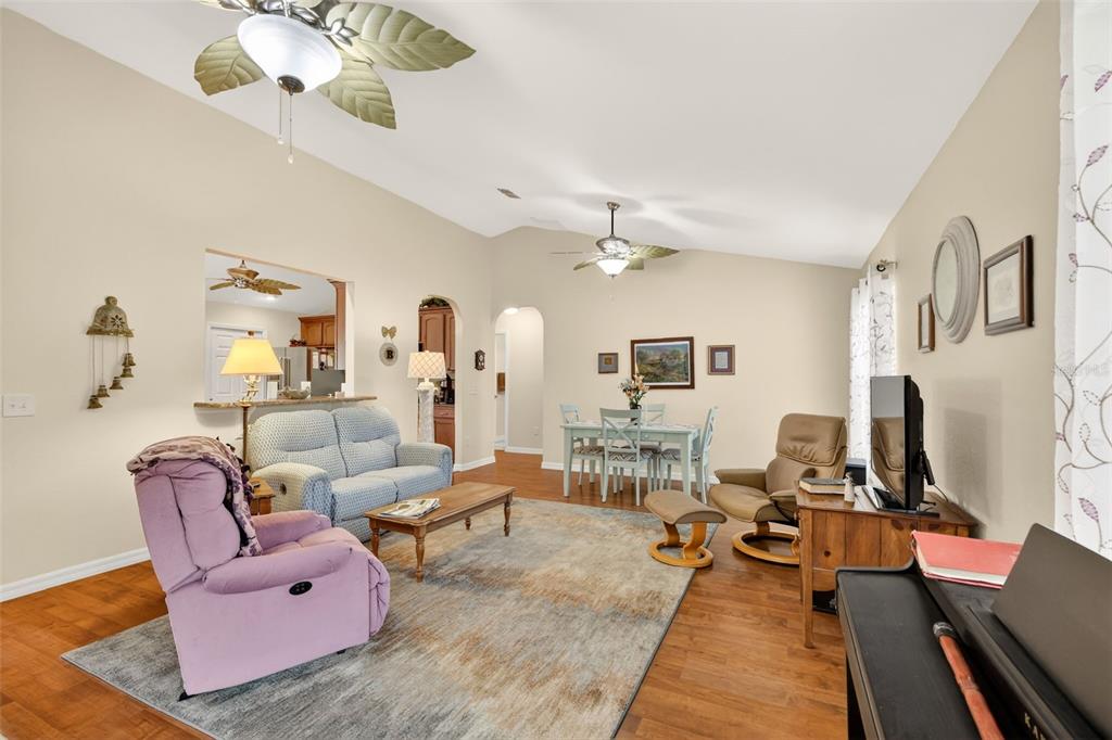 A living room with a vaulted ceiling, wood flooring, a ceiling fan, and dining area — 11217 SE 170TH LANE, SUMMERFIELD, FL