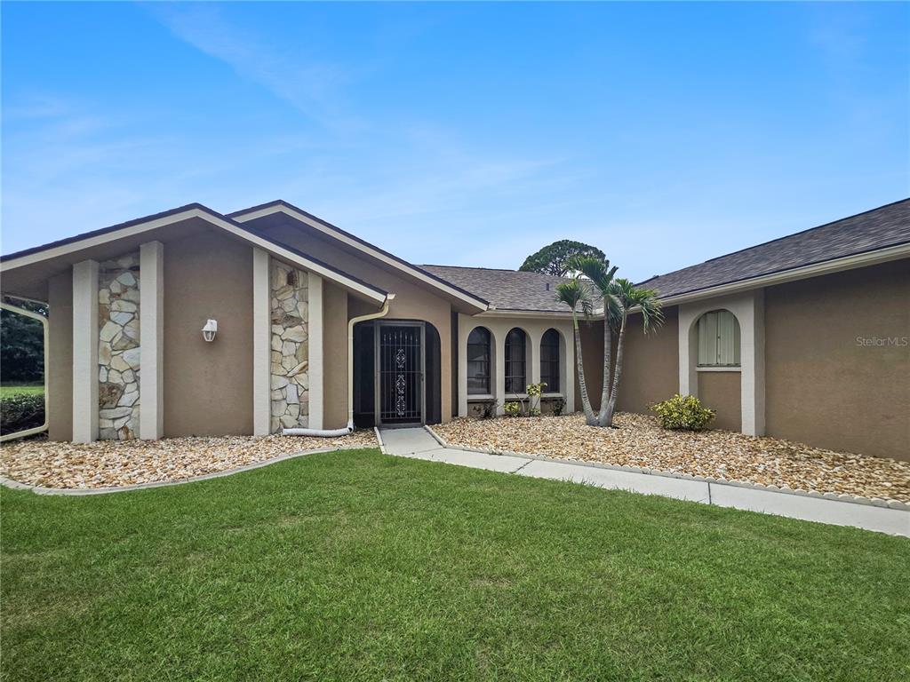 A single-story house with a brown stucco exterior, stone accents, and a front walkway — 26085 CONCEPCION DRIVE, PUNTA GORDA, FL
