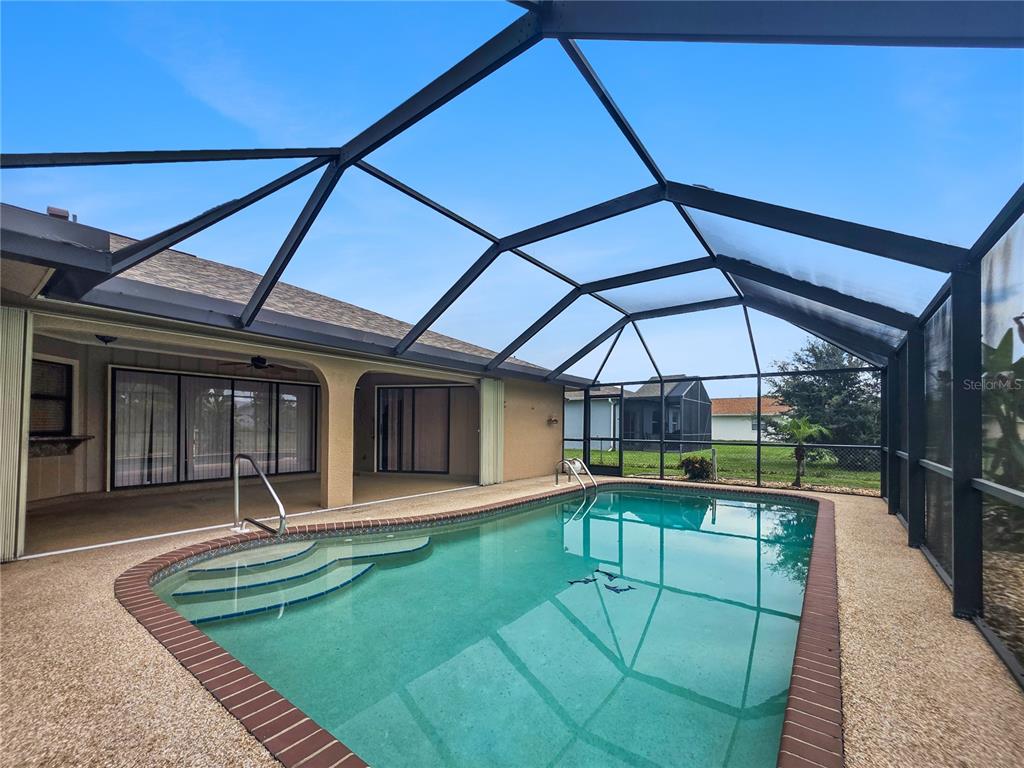 A swimming pool with steps is enclosed by a screened lanai attached to a house — 26085 CONCEPCION DRIVE, PUNTA GORDA, FL