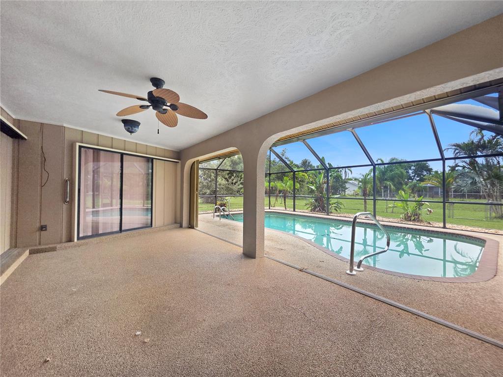 A covered patio features a textured floor, a ceiling fan, and a screened-in swimming pool — 26085 CONCEPCION DRIVE, PUNTA GORDA, FL