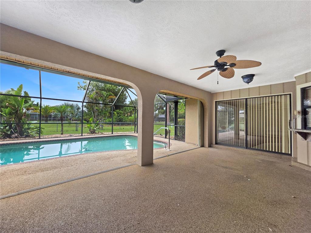 A covered patio with a ceiling fan overlooks a screened-in swimming pool and backyard — 26085 CONCEPCION DRIVE, PUNTA GORDA, FL