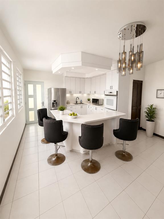 A white kitchen features a curved breakfast bar with three black stools and pendant lighting — 843 CAM LOS RAMOS, TRUJILLO ALTO, PR