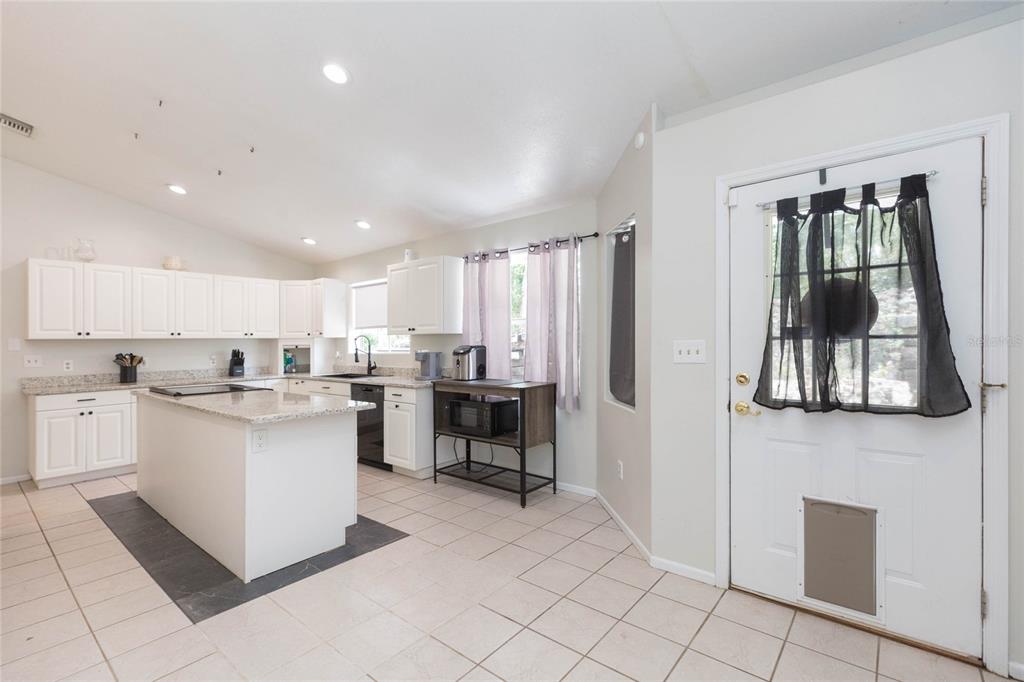 A kitchen with white cabinets, a granite-topped island, tile flooring, and a white entry door — 34299 BELT DRIVE, DADE CITY, FL