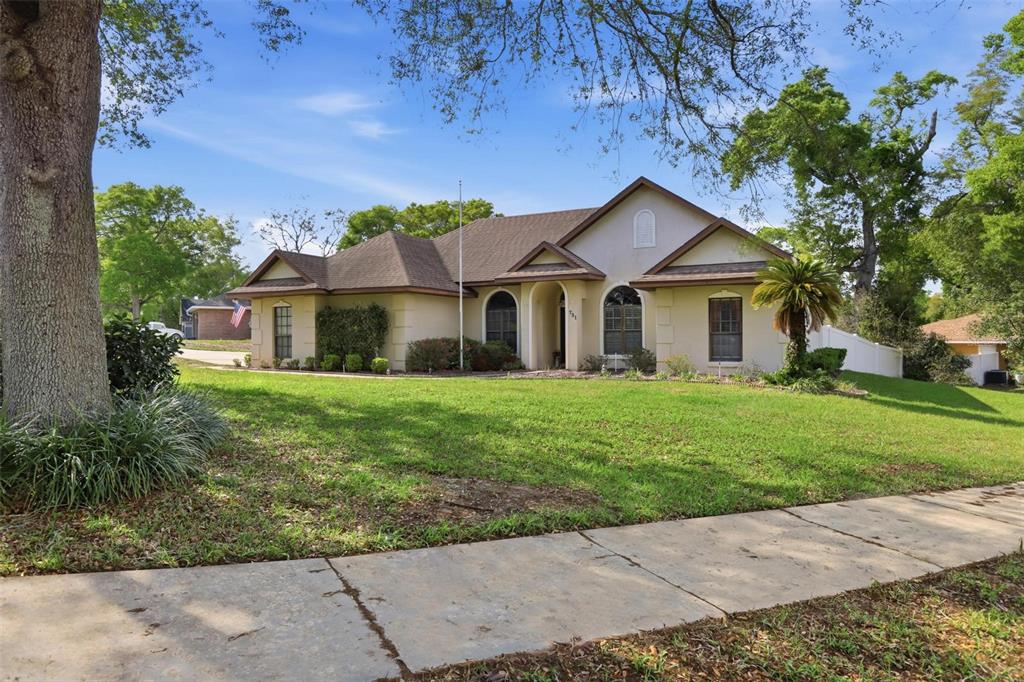 A single-story house with a beige stucco exterior, brown roof, and a large front lawn — 731 EDGEWILD COURT, ORANGE CITY, FL
