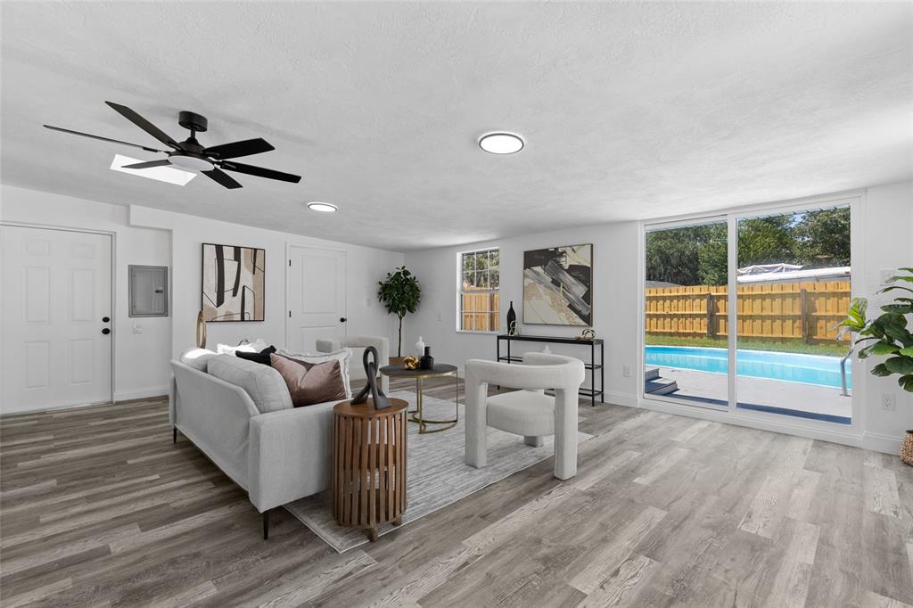 A living room with wood-look flooring, a ceiling fan, and sliding doors overlooking a pool — 1259 SCOTTSDALE DRIVE, ORMOND BEACH, FL