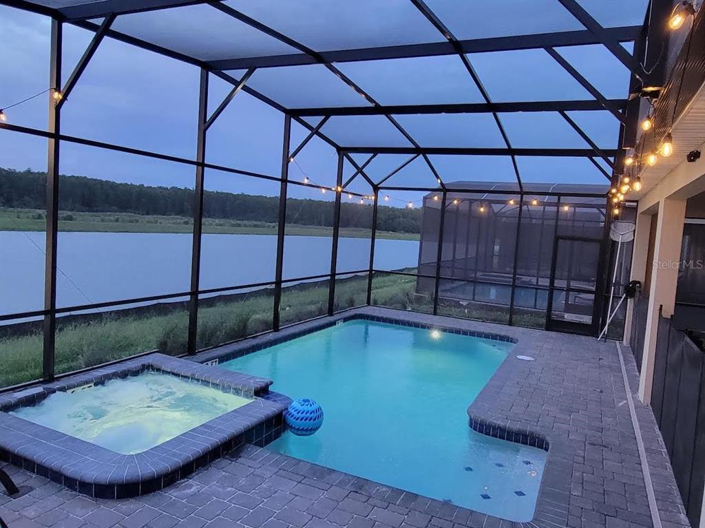 A screened-in pool and hot tub overlook a lake at dusk — 4173 PARAGRAPH DRIVE, KISSIMMEE, FL