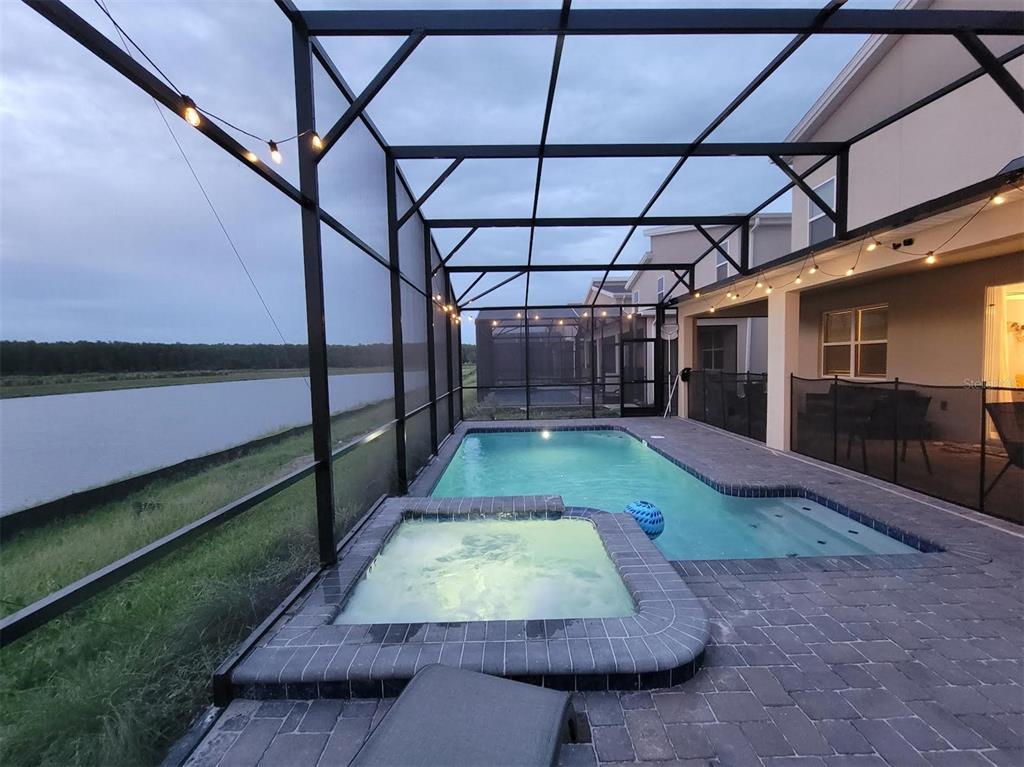 A screened-in patio features a swimming pool, a hot tub, and a view of water — 4173 PARAGRAPH DRIVE, KISSIMMEE, FL