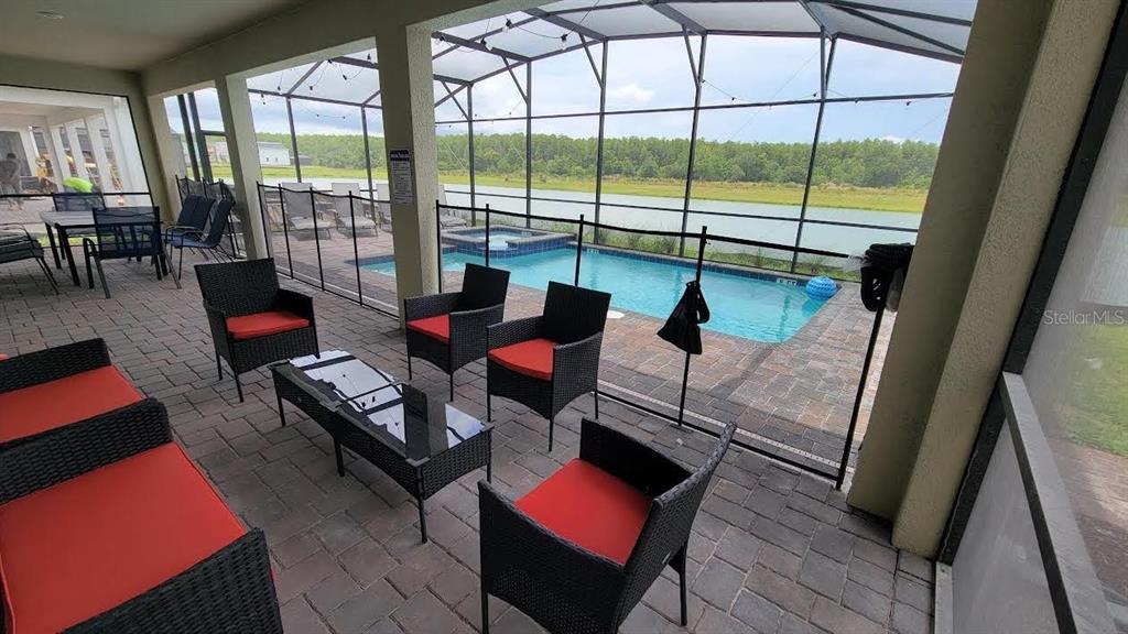 A covered patio features outdoor furniture, a pool with a spa, and a lake view — 4173 PARAGRAPH DRIVE, KISSIMMEE, FL