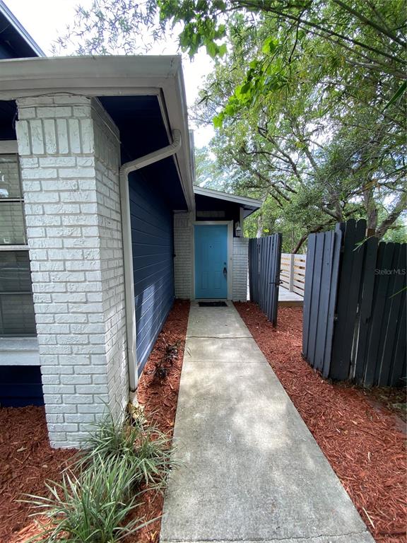 A concrete walkway leads to a light blue front door beside a white brick wall — 7222 NIMA COURT, ORLANDO, FL