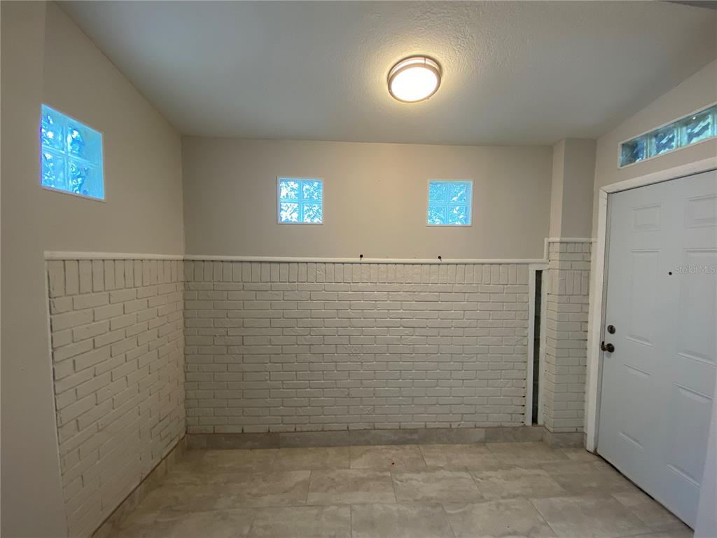A room with white painted brick walls, glass block windows, and light-colored tile flooring — 7222 NIMA COURT, ORLANDO, FL