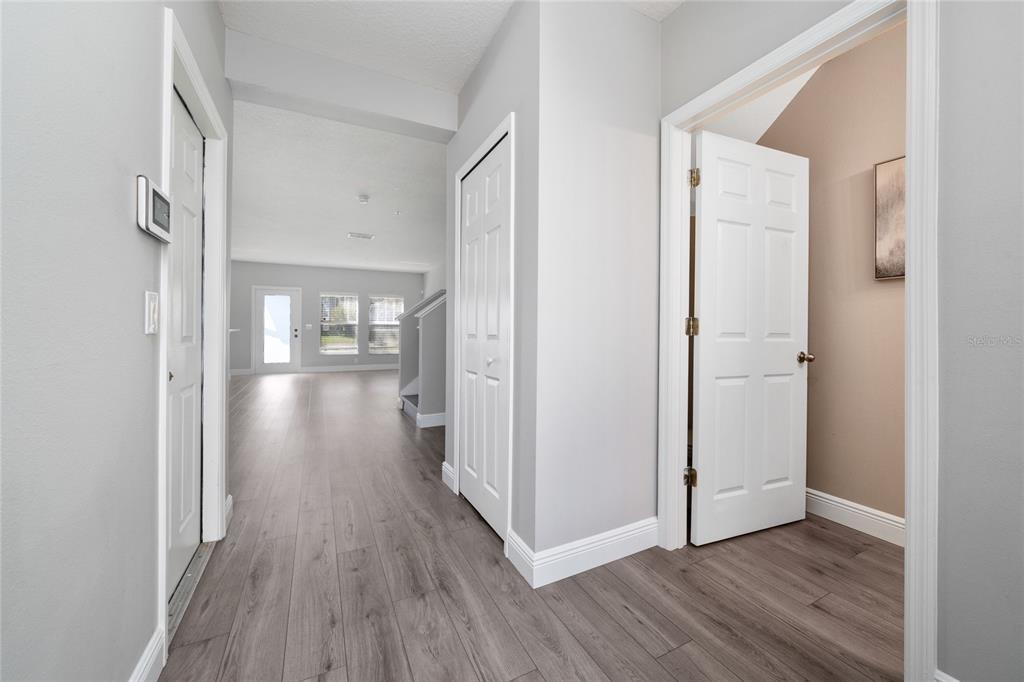 A hallway with light wood-look flooring leads to an open living area with white doors — 5412 CARAMELLA DRIVE, ORLANDO, FL