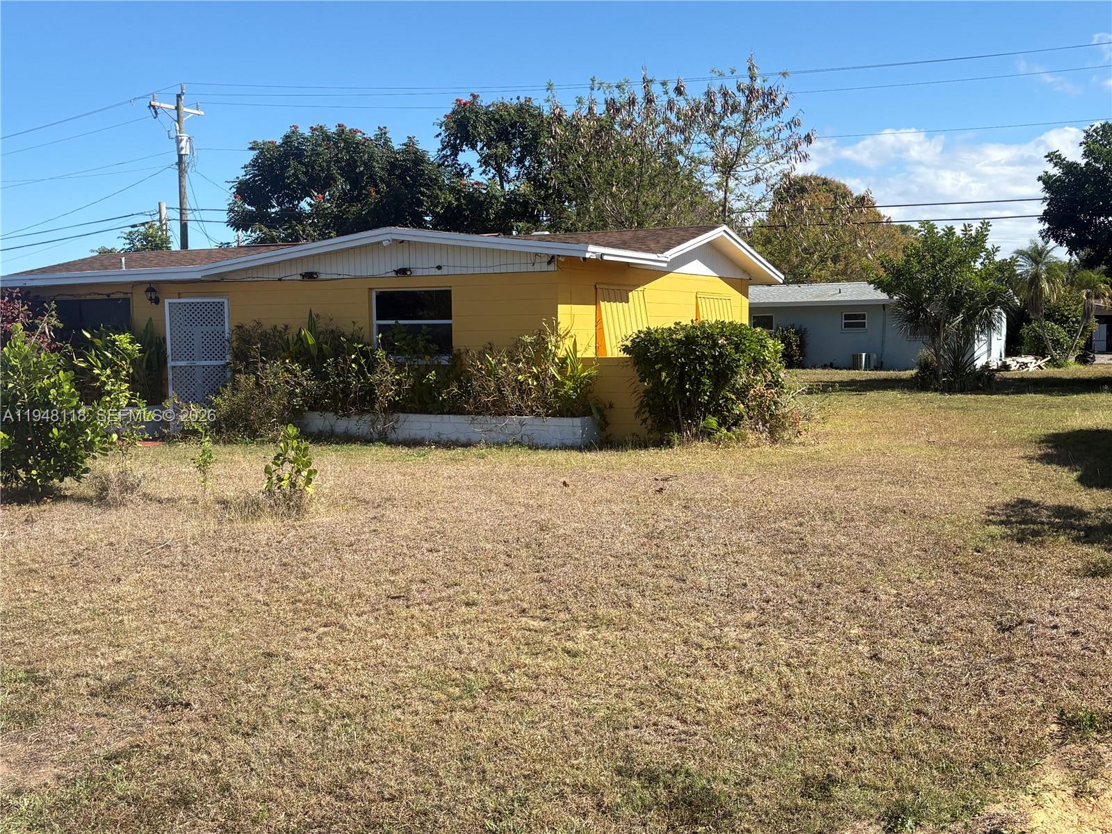 A yellow single-story house sits on a large, dry grass lot under a blue sky — 108 Coolidge ave, Lehigh Acres FL 33936, LEHIGH ACRES, FL