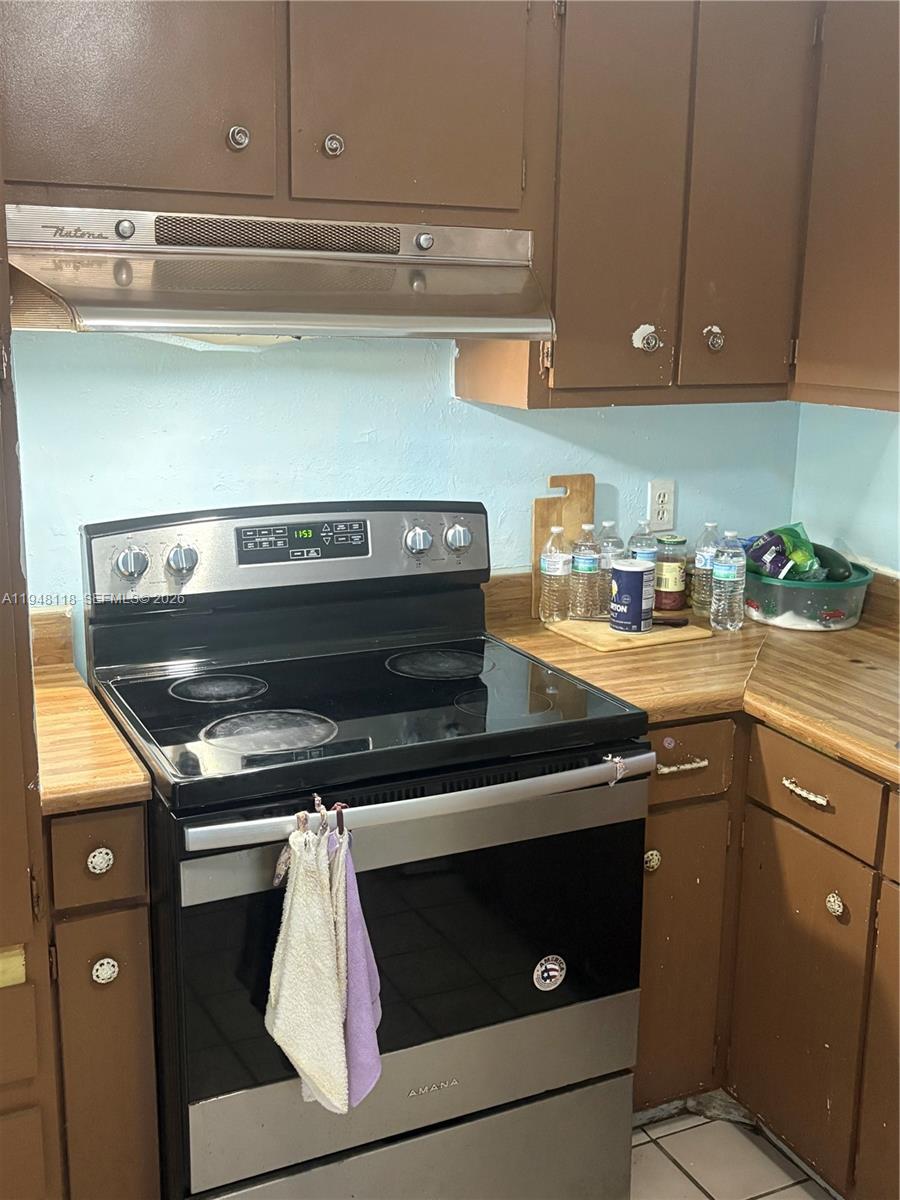 A kitchen features brown cabinets, a stainless steel Amana electric range, and a Nutone hood — 108 Coolidge ave, Lehigh Acres FL 33936, LEHIGH ACRES, FL