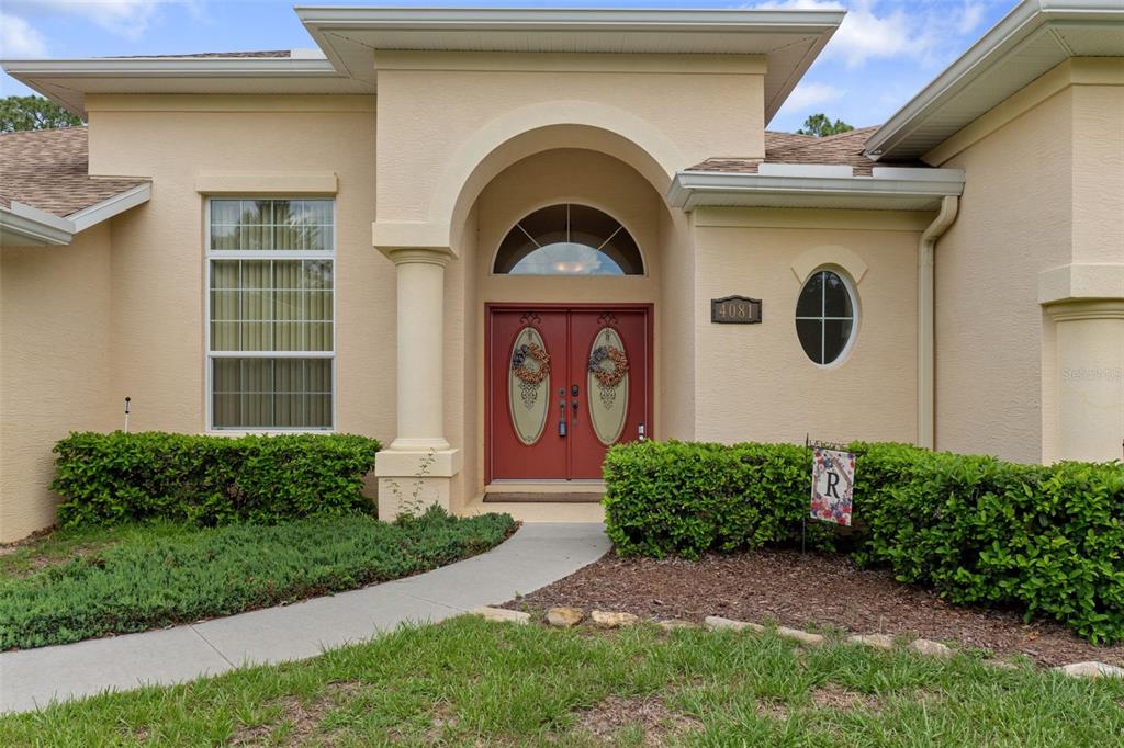 A beige house exterior features a red double front door under an arched entryway — 4081 W ROUNDUP COURT, BEVERLY HILLS, FL