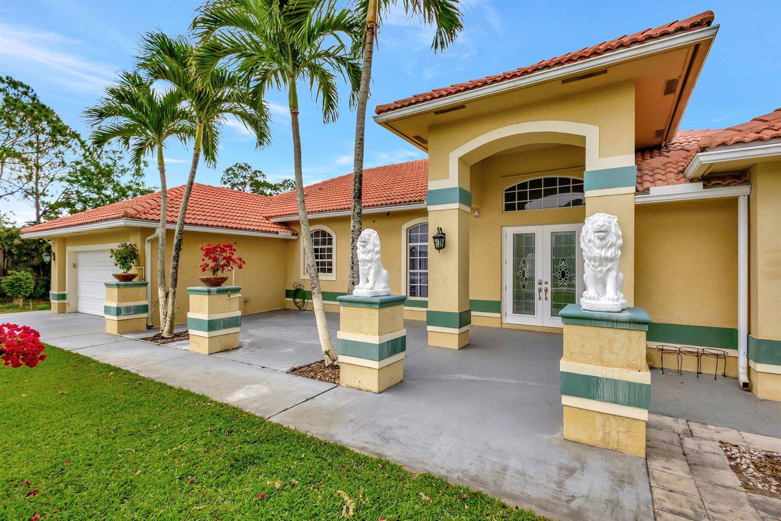 A yellow house with a tile roof, palm trees, and two lion statues on pedestals — 12402 83rd Lane N, FL 33412, FL