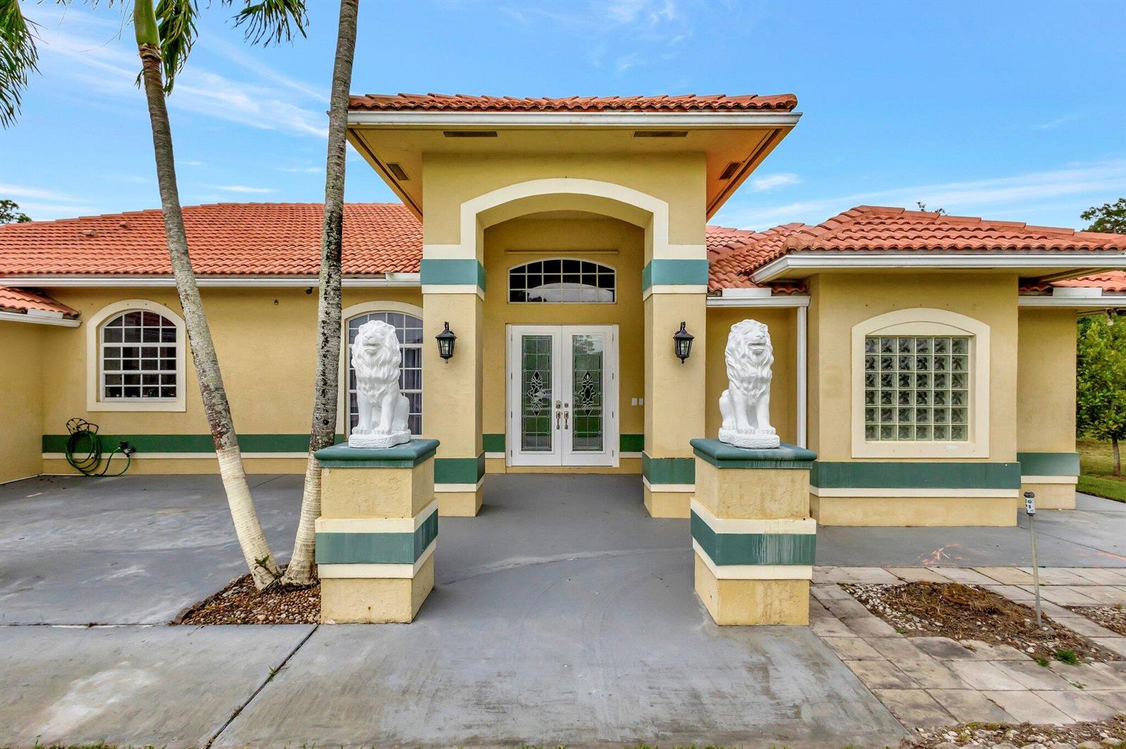 A yellow house with a tiled roof, two lion statues, and a double-door entrance — 12402 83rd Lane N, FL 33412, FL