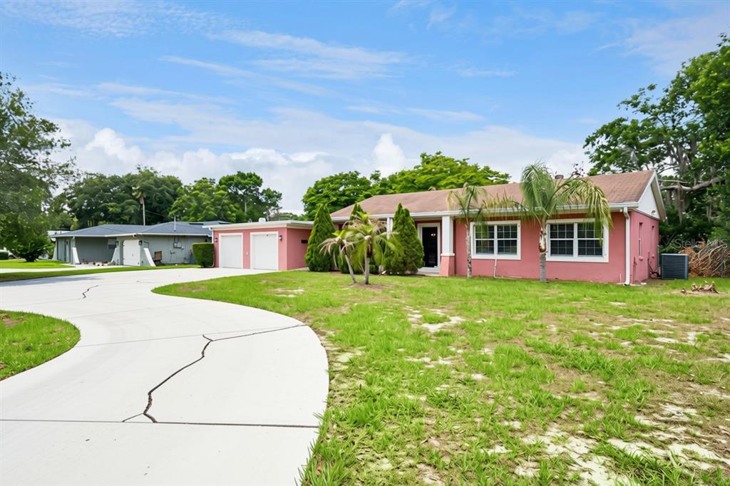 A pink house exterior features a white garage door, a front door, and a conifer tree — 78 S WINTER PARK DRIVE, CASSELBERRY, FL